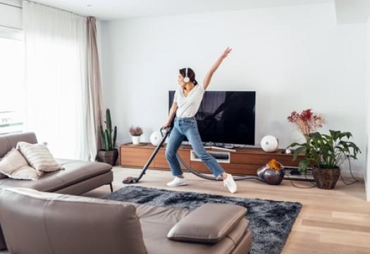 Young woman listening to music and dancing around the living room while vacuuming. She is having fun while tidying up her home. | Merry Maids®