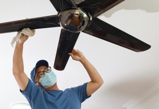 Low-angle view of an Asian man cleaning ceiling fan at home | Merry Maids