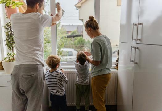 Young children helping their parents with chores in the morning before school. They are helping wipe down windows while watching for the school bus. | Merry Maids